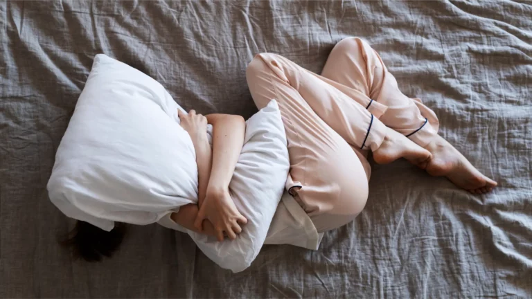 Femme allongée lit gris blanc vue de dessus, illustrant troubles sommeil ménopause : insomnie, interruptions sommeil, fatigue chronique liés fluctuations hormonales œstrogène baisse densité osseuse