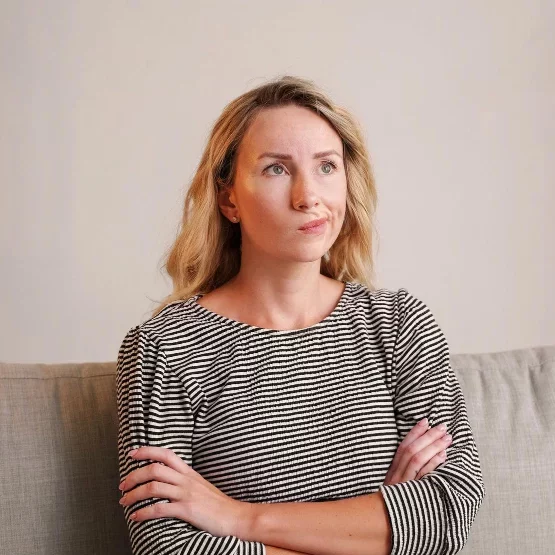 Femme d'une cinquantaine d'années assise sur un canapé, bras croisés et regard pensif, illustrant la fatigue hormonale et le manque d'énergie liés à la ménopause