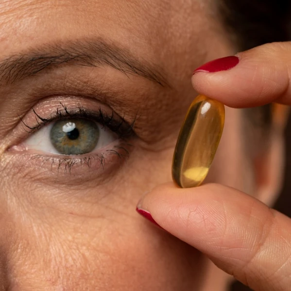 Gros plan sur le visage d'une femme mature tenant entre ses doigts une capsule de complément alimentaire, illustrant le guide comparatif pour choisir les meilleurs compléments alimentaires à la ménopause