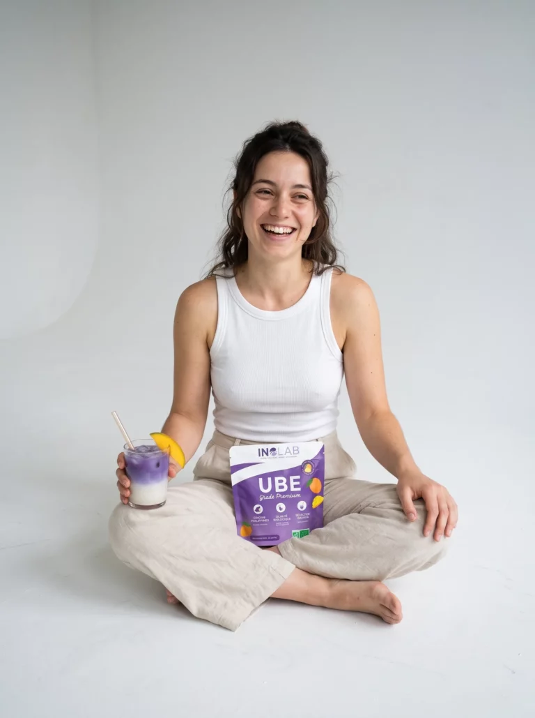 Femme souriante assise au sol avec un verre d'ube latte à la mangue et un pochon d'Ube Mangue Inolab